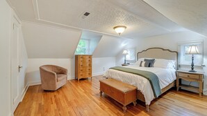 Quarto com piso de madeira, cama com cabeceira, mesa de cabeceira, cômoda, cadeira e janela com persianas.