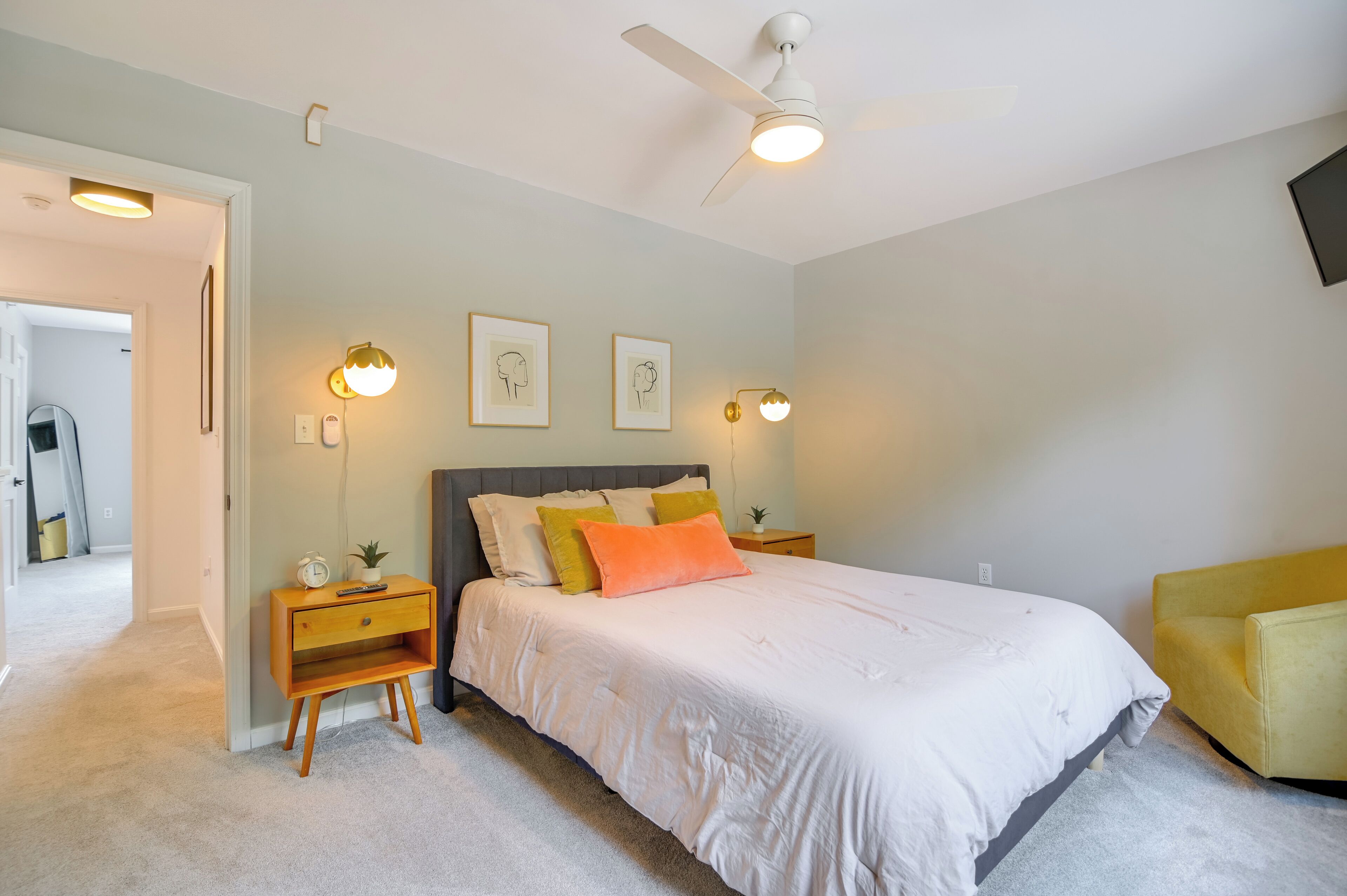 Un dormitorio con cama, mesitas de noche, ventilador de techo, luces fijadas en la pared y cuadros enmarcados.