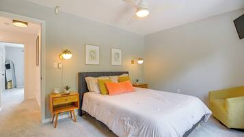 Un dormitorio con cama, mesitas de noche, ventilador de techo, luces fijadas en la pared y cuadros enmarcados.
