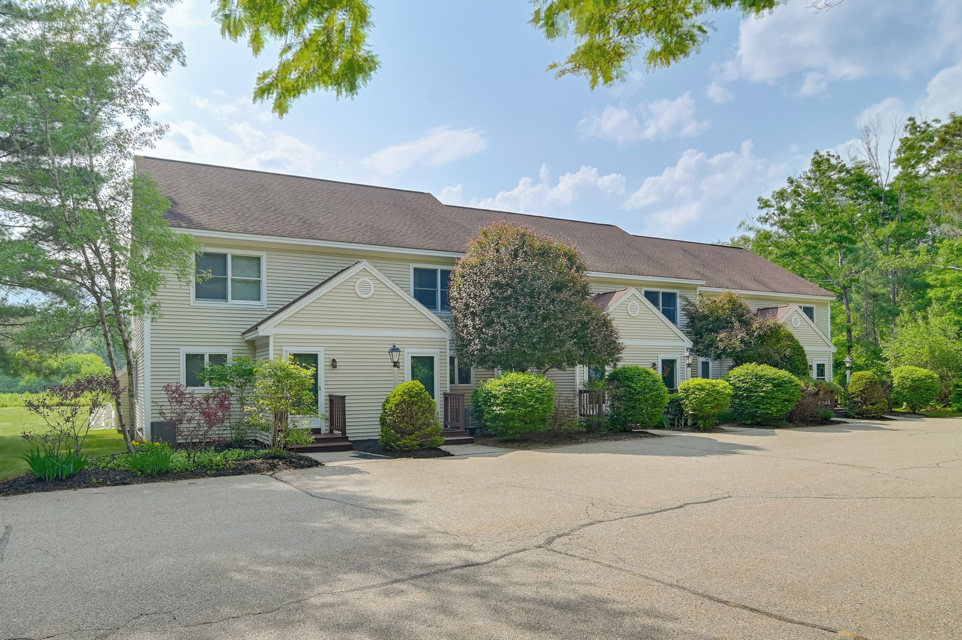A two-story residential building with a driveway, surrounded by well-maintained landscaping and trees.