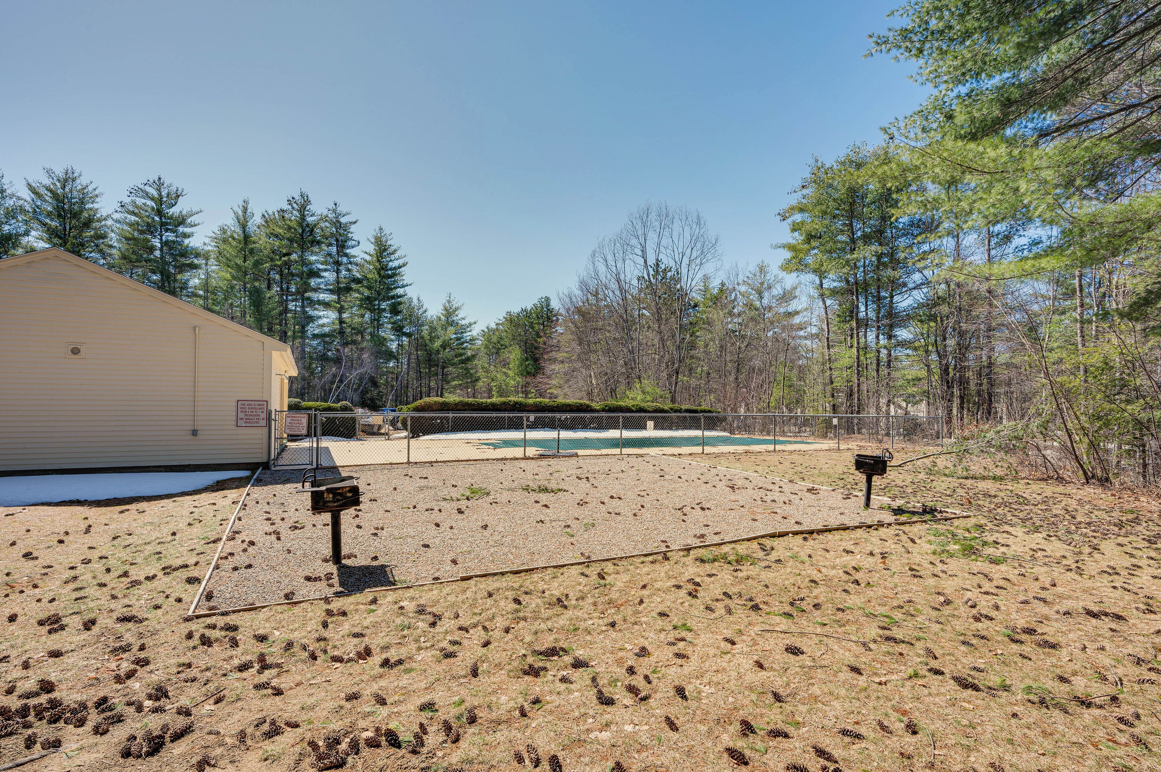 A building with a fenced outdoor area, a small pool, and a wooded backdrop.