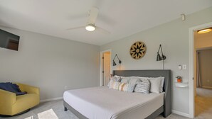 A bedroom with a bed, a chair, a ceiling fan, a wall-mounted TV, and a door leading to another room. - North Conway Home for Fall Adventures (North Conway)