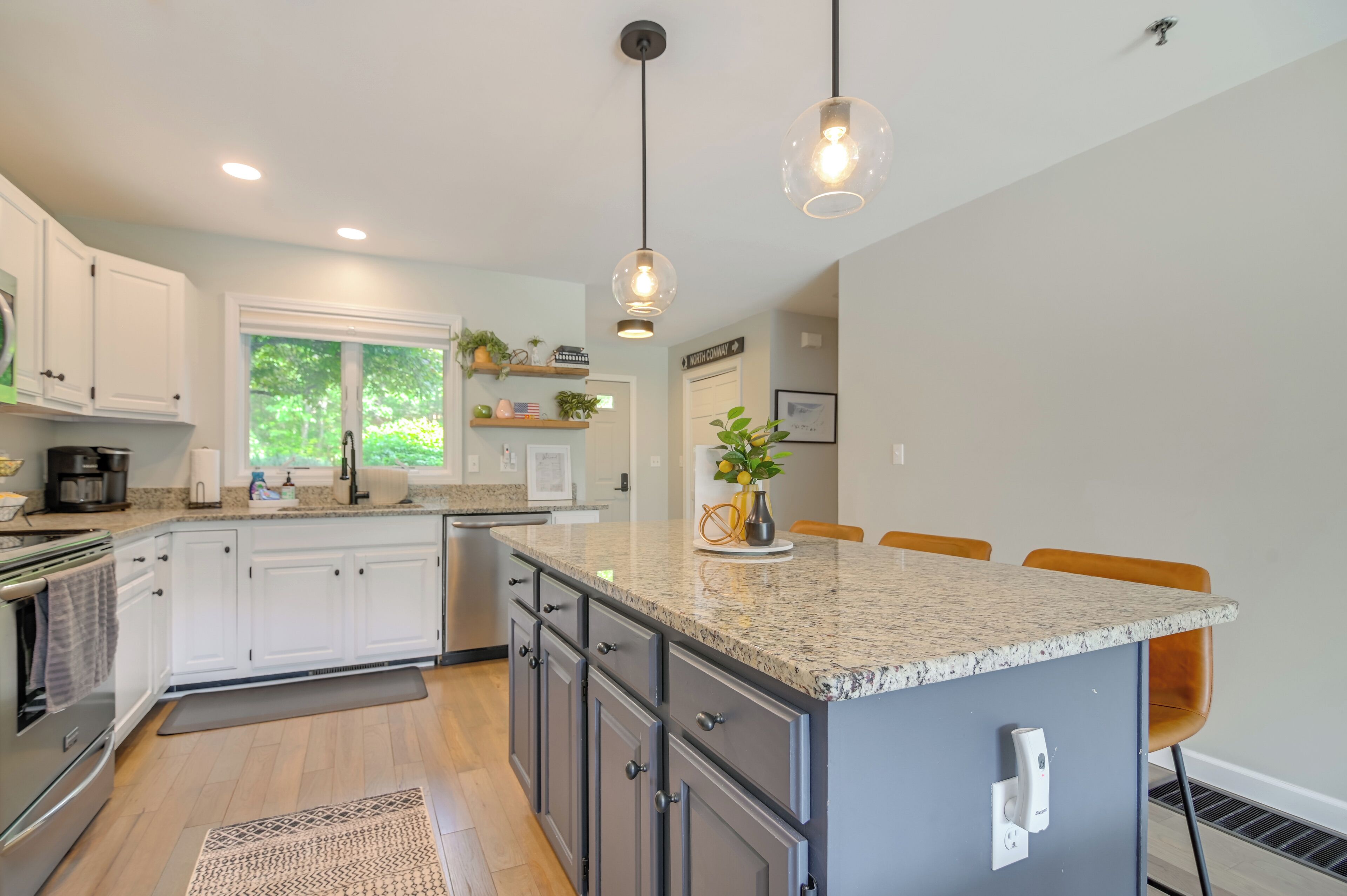 A modern kitchen with white cabinets, granite countertops, and pendant lighting.