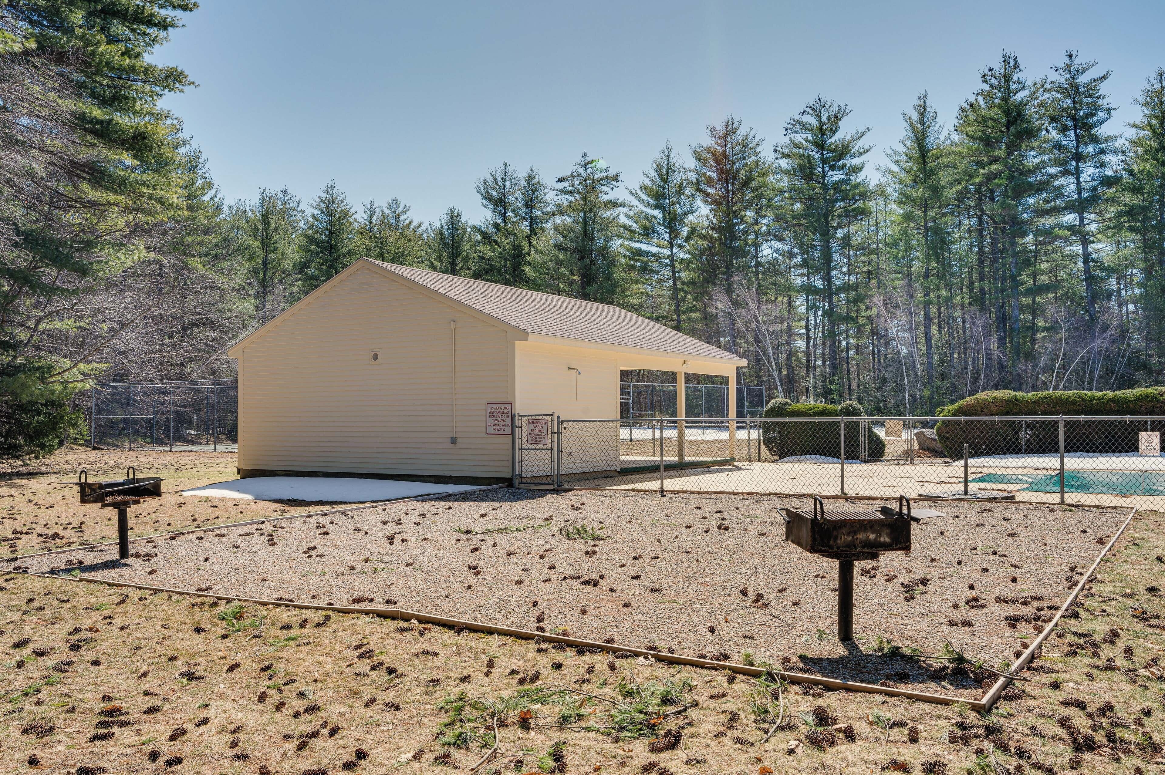 A small, single-story building with a flat roof, surrounded by a fenced area with a pool and dense pine trees in the background.