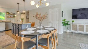 A modern kitchen with a dining area, wooden chairs, a round table with a white placemat, pendant lights, and a TV mounted on the wall. - North Conway Home for Fall Adventures (North Conway)