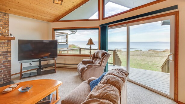 Ein gemütliches Wohnzimmer mit einem großen Fernseher, bequemen Sitzgelegenheiten und Blick auf den Strand.