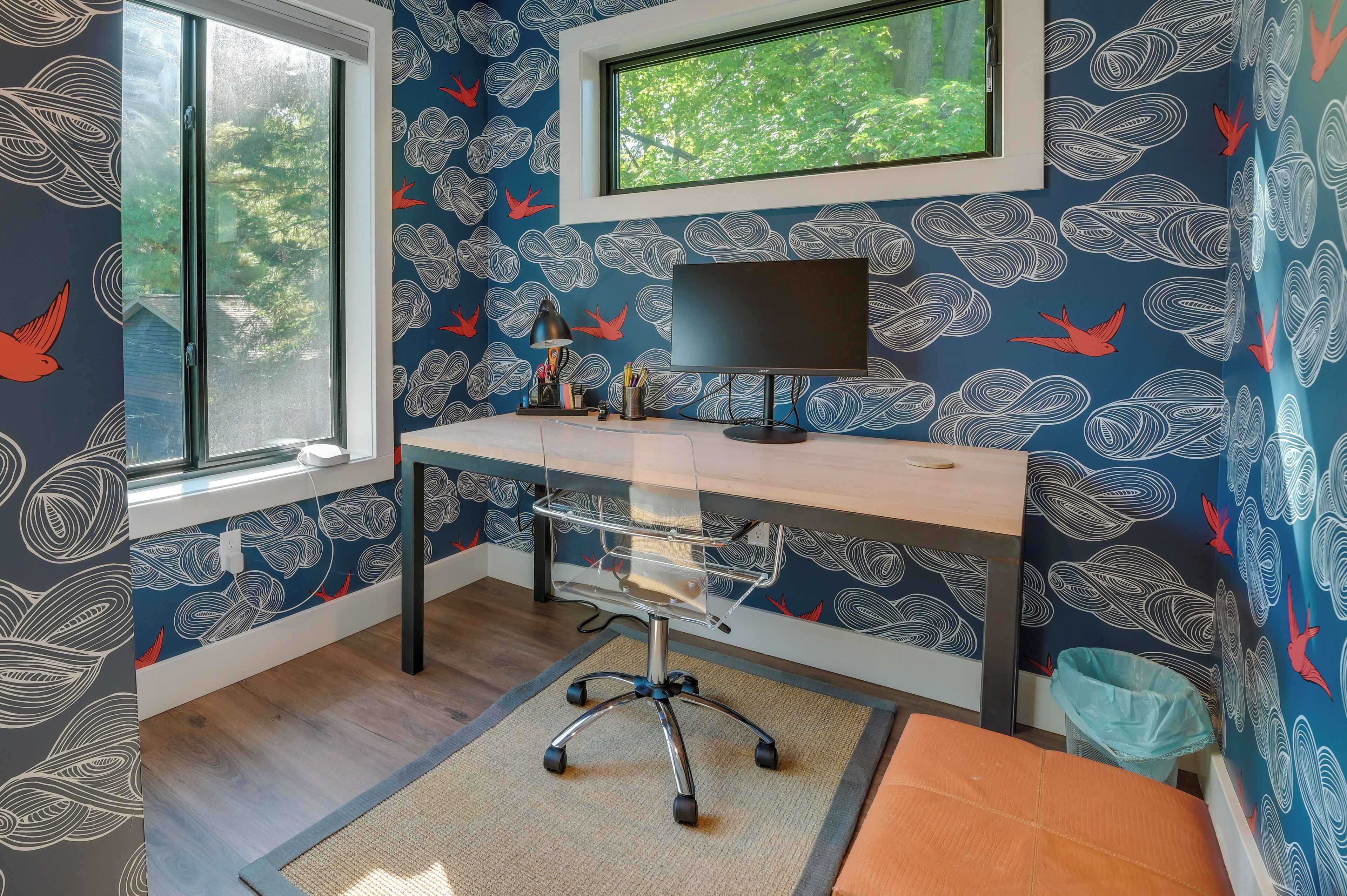 A room with a desk, a computer, a window, and a view of greenery outside.