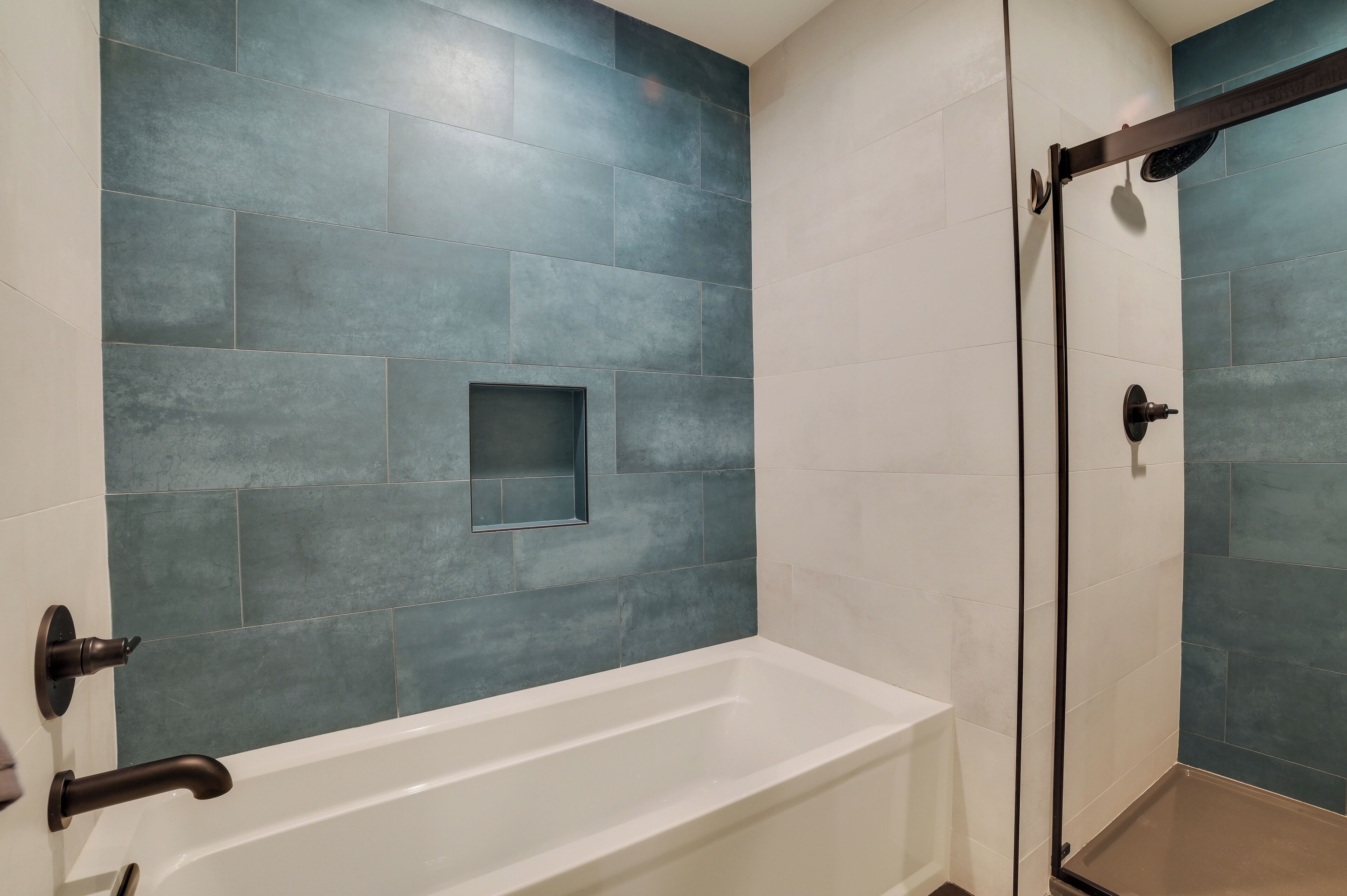 A modern bathroom with a white bathtub, a glass shower enclosure, and blue-tiled walls.