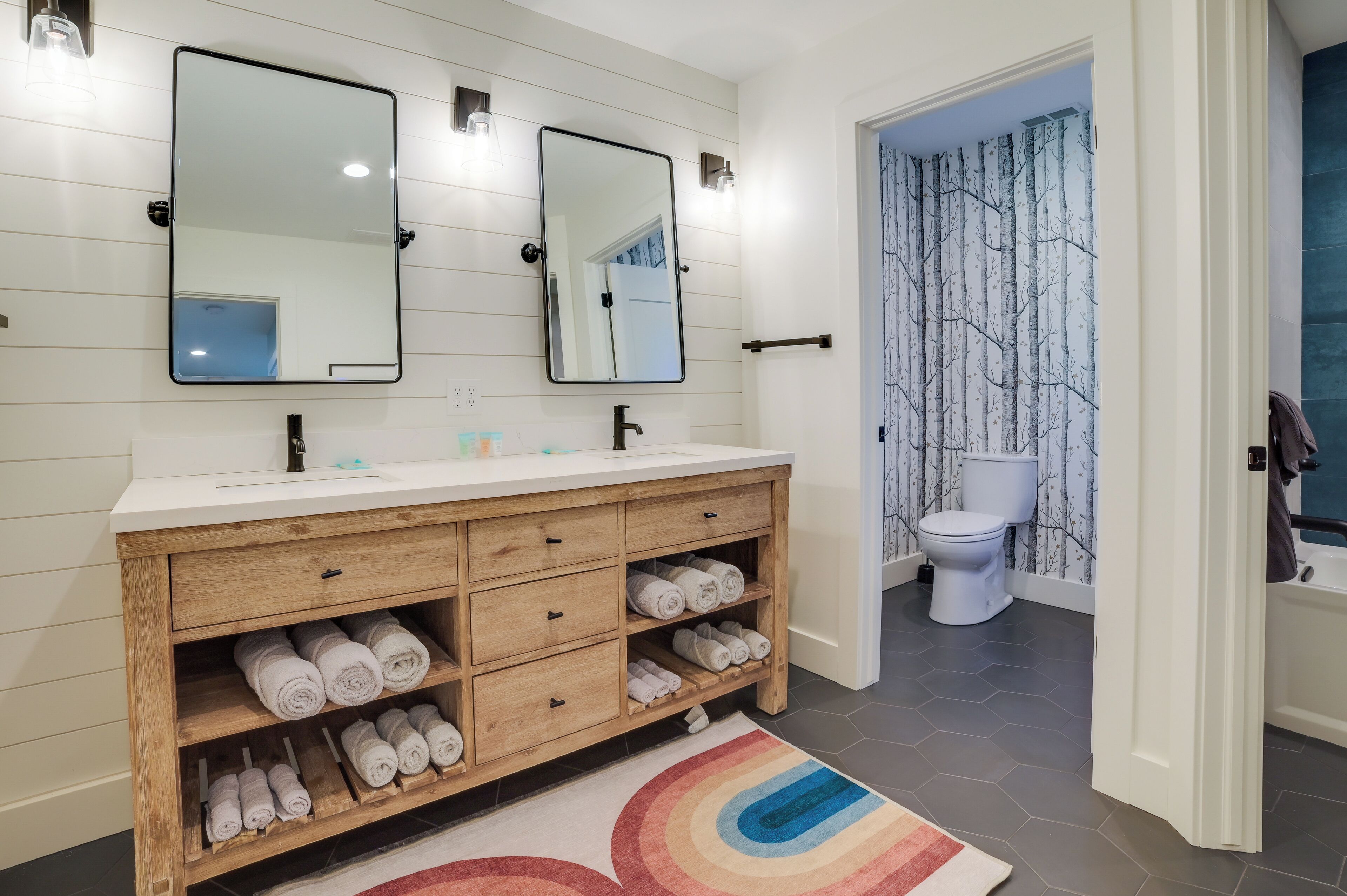 A modern bathroom with a wooden vanity, two mirrors, and a white toilet.