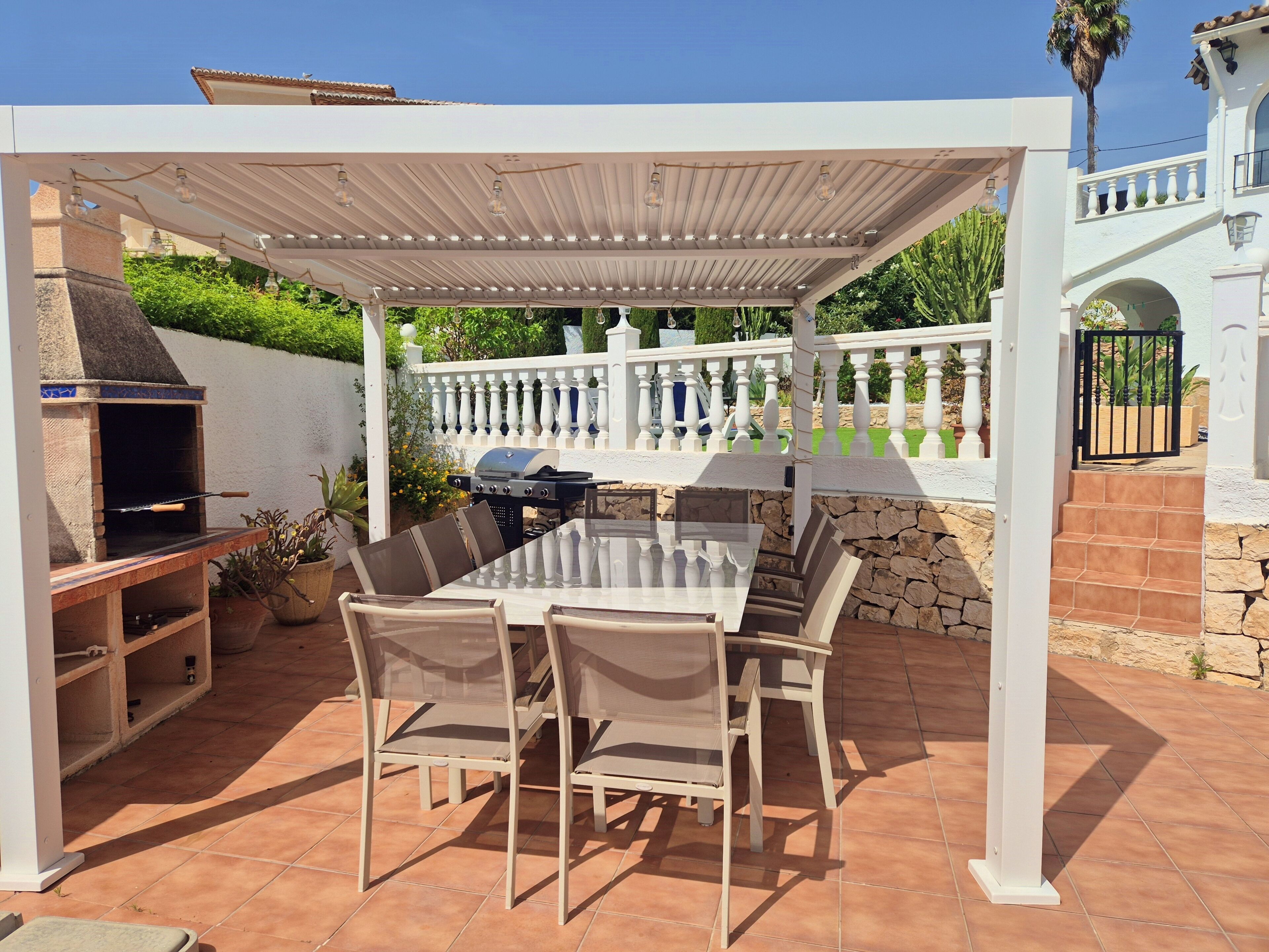 An outdoor patio with a pergola, a barbecue grill, and a dining table with chairs.