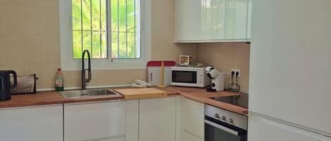 A kitchen with white cabinets, a microwave, an oven, a sink, and a window with a view of palm trees.