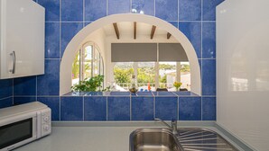A kitchen with blue tiles, a stainless steel sink, and a microwave.