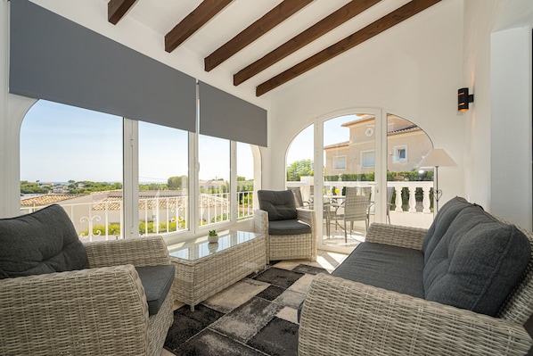 A sunlit room with wicker furniture, large windows, and a view of the surrounding area. - Schöne Villa für 10 pax in der Nähe von Moraira mit Privatem Pool und Meerblick (Teulada)