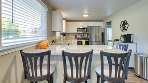 A modern kitchen with a central island, white cabinets, stainless steel appliances, and a window with blinds.