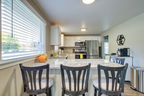 Una cocina moderna con armarios blancos, una isla central con taburetes de bar, electrodomésticos de acero inoxidable y vistas amplias a través de grandes ventanales.