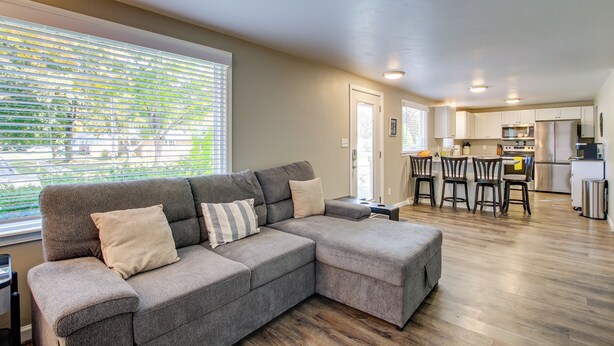 A modern living room with a sectional sofa, a dining area with chairs, and a kitchen in the background.