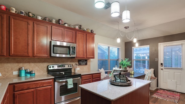 A kitchen with wooden cabinets, stainless steel appliances, and a central island. - Patio, Pergola & Pool Access: Aubrey Retreat! (Aubrey)