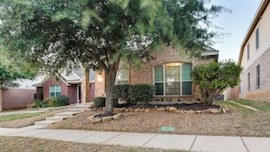 A two-story brick house with a front yard, a small tree, and a pathway leading to the entrance. - Patio, Pergola & Pool Access: Aubrey Retreat! (Aubrey)