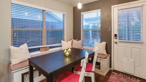 A dining area with a dark wooden table, white chairs with red cushions, and a bench with a patterned cushion. - Patio, Pergola & Pool Access: Aubrey Retreat! (Aubrey)