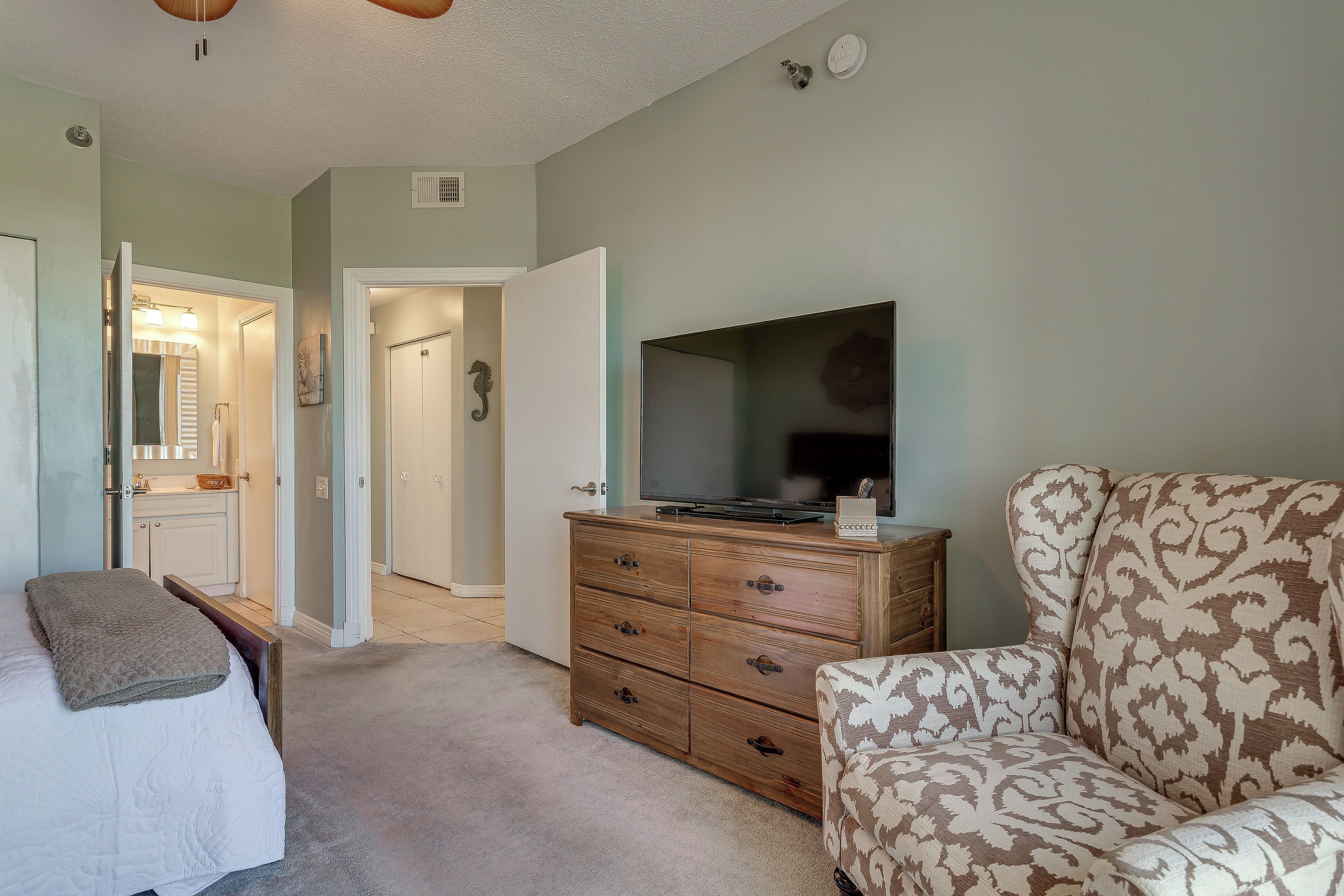 A bedroom with a bed, a dresser, a television, and a patterned armchair.