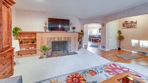 A spacious living room with a fireplace, a flat-screen TV mounted above it, and a dining area in the background. - Enchanting Puyallup Home w/ Spacious Deck! (Puyallup)