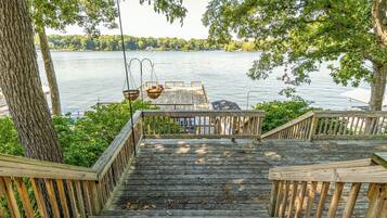 A wooden deck with a view of a lake, a hanging chair, and a table.