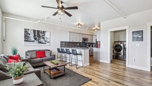A modern apartment with a living room, kitchen, and dining area. It includes a ceiling fan, bar stools, a coffee table, and a potted plant. - Mountain-view Deck: Stylish Virginia City Apt! (Virginia City)