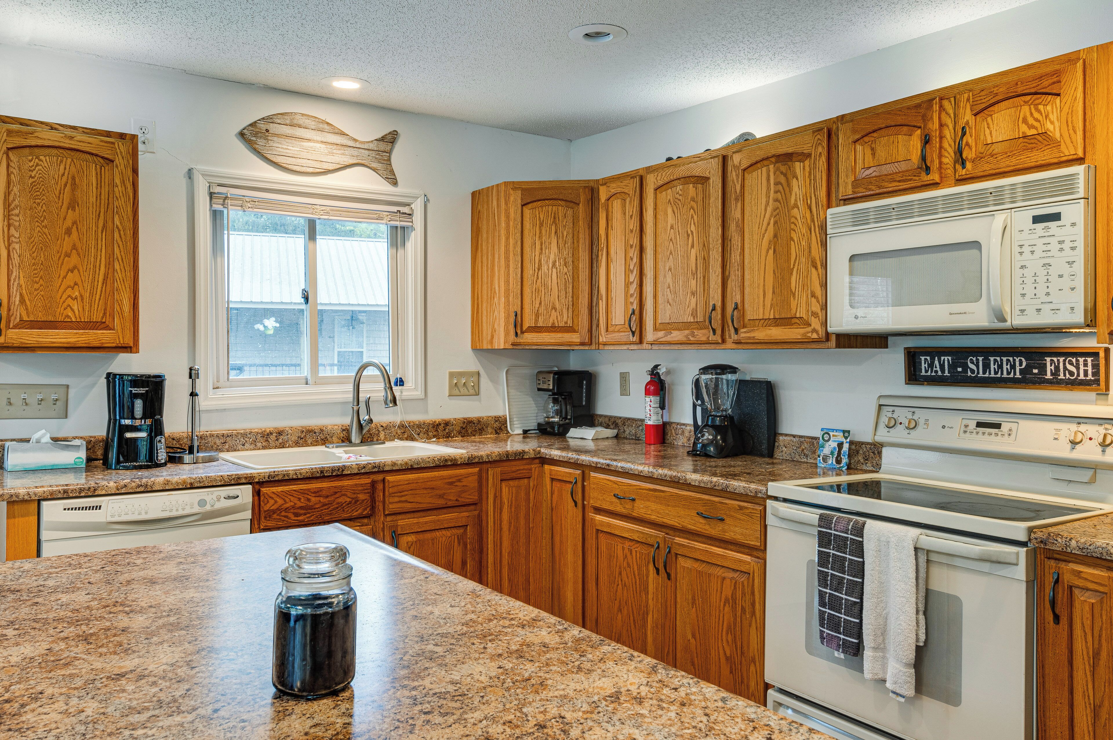 A kitchen with wooden cabinets, granite countertops, a microwave, a stove, and a coffee maker.