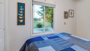 A bedroom with a large window, a blue and gray quilt, and two framed pictures on the wall. - Riverfront Brookston Retreat w/ Deck & River Tubes (Brookston)