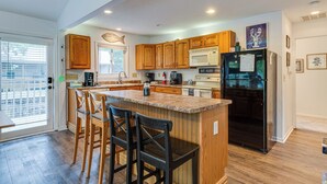 A modern kitchen with wooden cabinets, a black refrigerator, and a granite countertop. - Riverfront Brookston Retreat w/ Deck & River Tubes (Brookston)