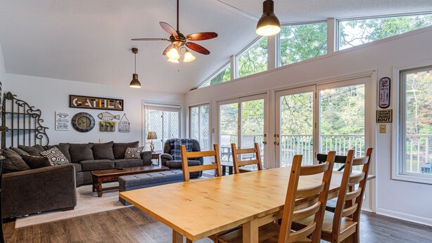 A spacious living area with a wooden dining table, dark sofas, and a ceiling fan. - Riverfront Brookston Retreat w/ Deck & River Tubes (Brookston)