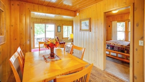 Un interno in legno con un tavolo da pranzo, sedie, un vaso con fiori e un letto con copripiumino trapuntato.