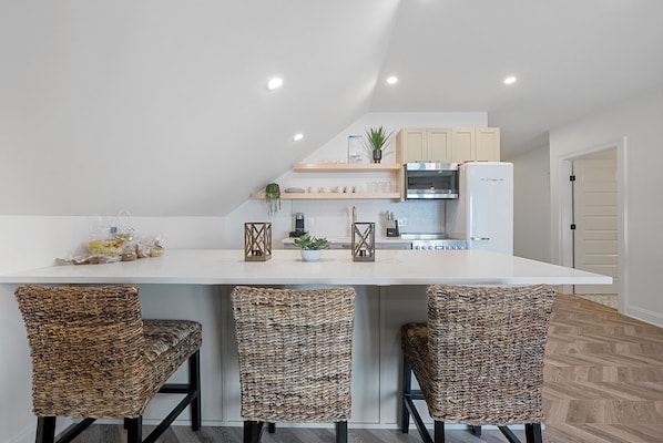 Une cuisine moderne avec un plan de travail blanc, trois chaises en osier et un four encastré.