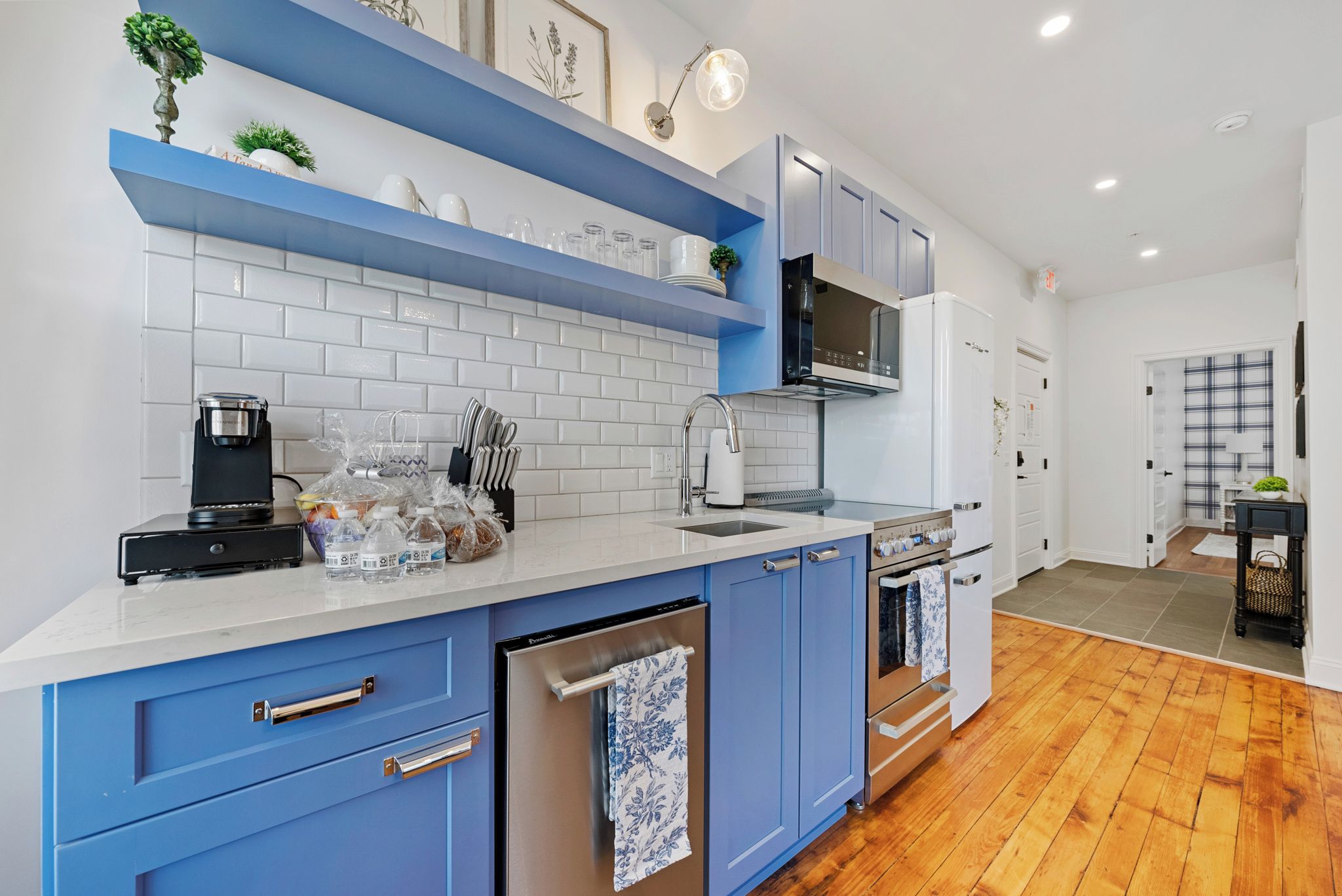 A modern kitchen with blue cabinets, white countertops, and stainless steel appliances.