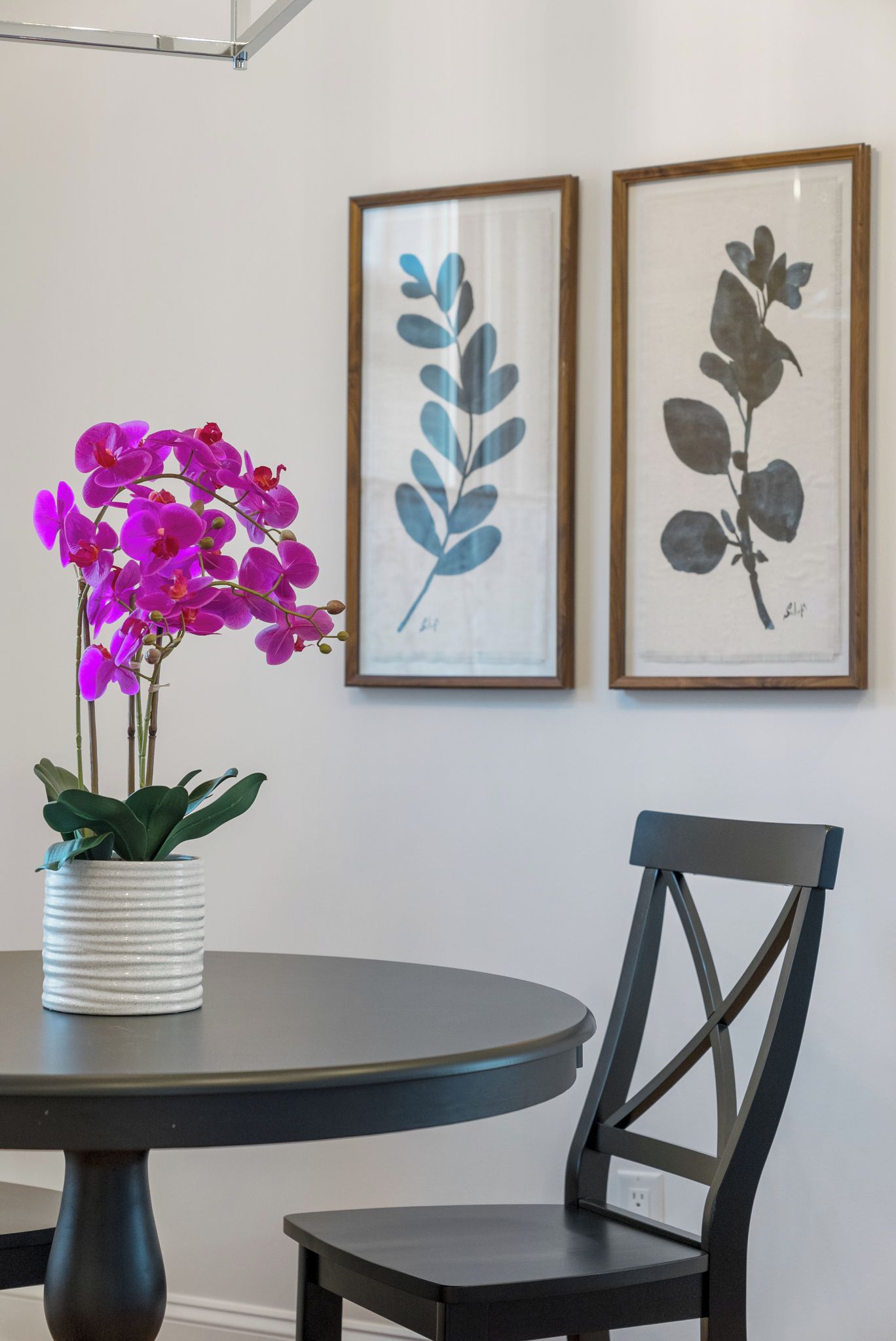 A dining area with a round table, a chair, and a potted orchid.