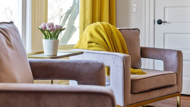 A modern living room with a sofa, a small table with a vase of flowers, and a yellow throw blanket. - Stylish Boutique Style Condo (Sandusky)