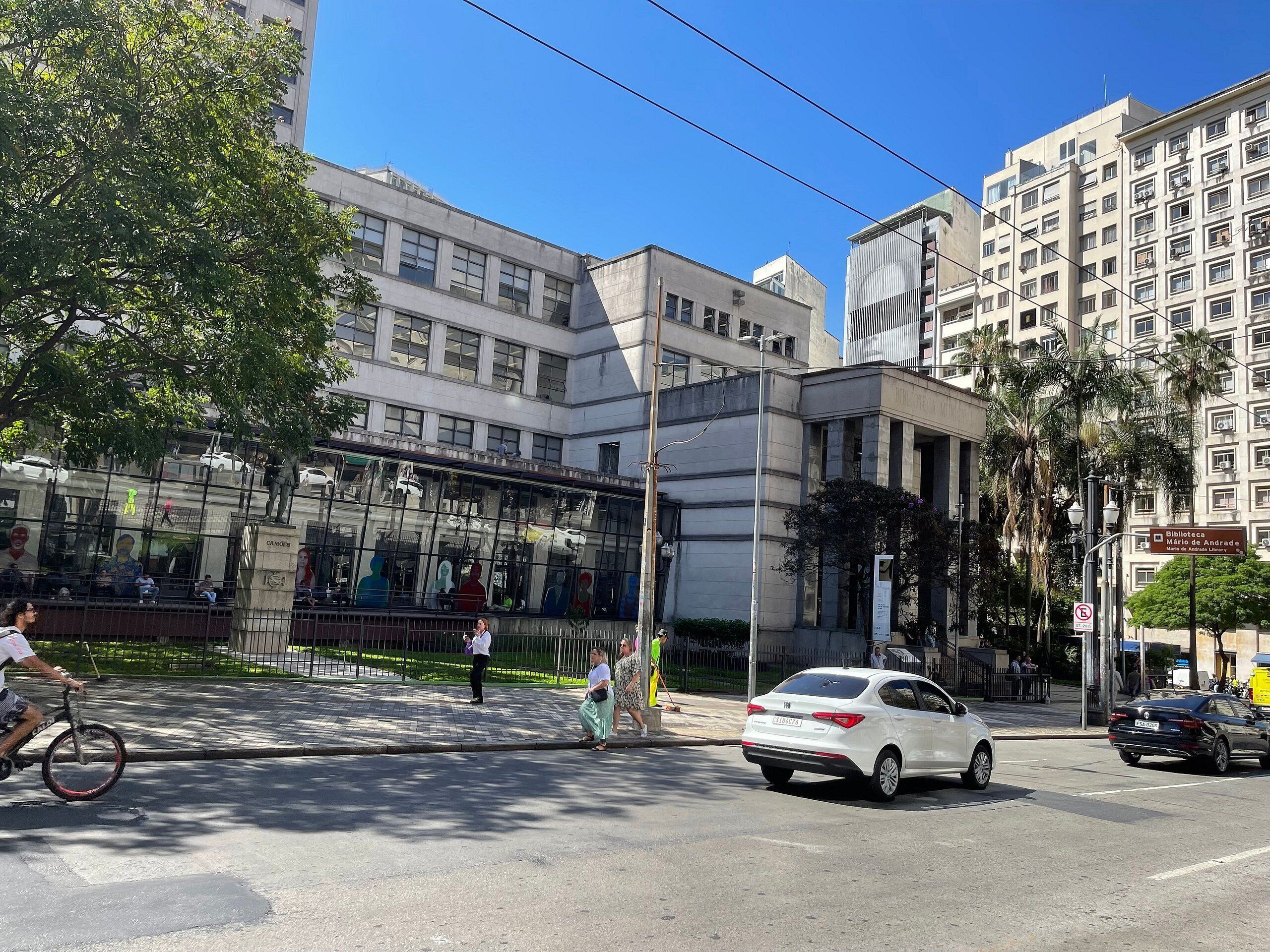 Une scène de rue avec un bâtiment moderne doté de grandes fenêtres et d’une façade en verre.