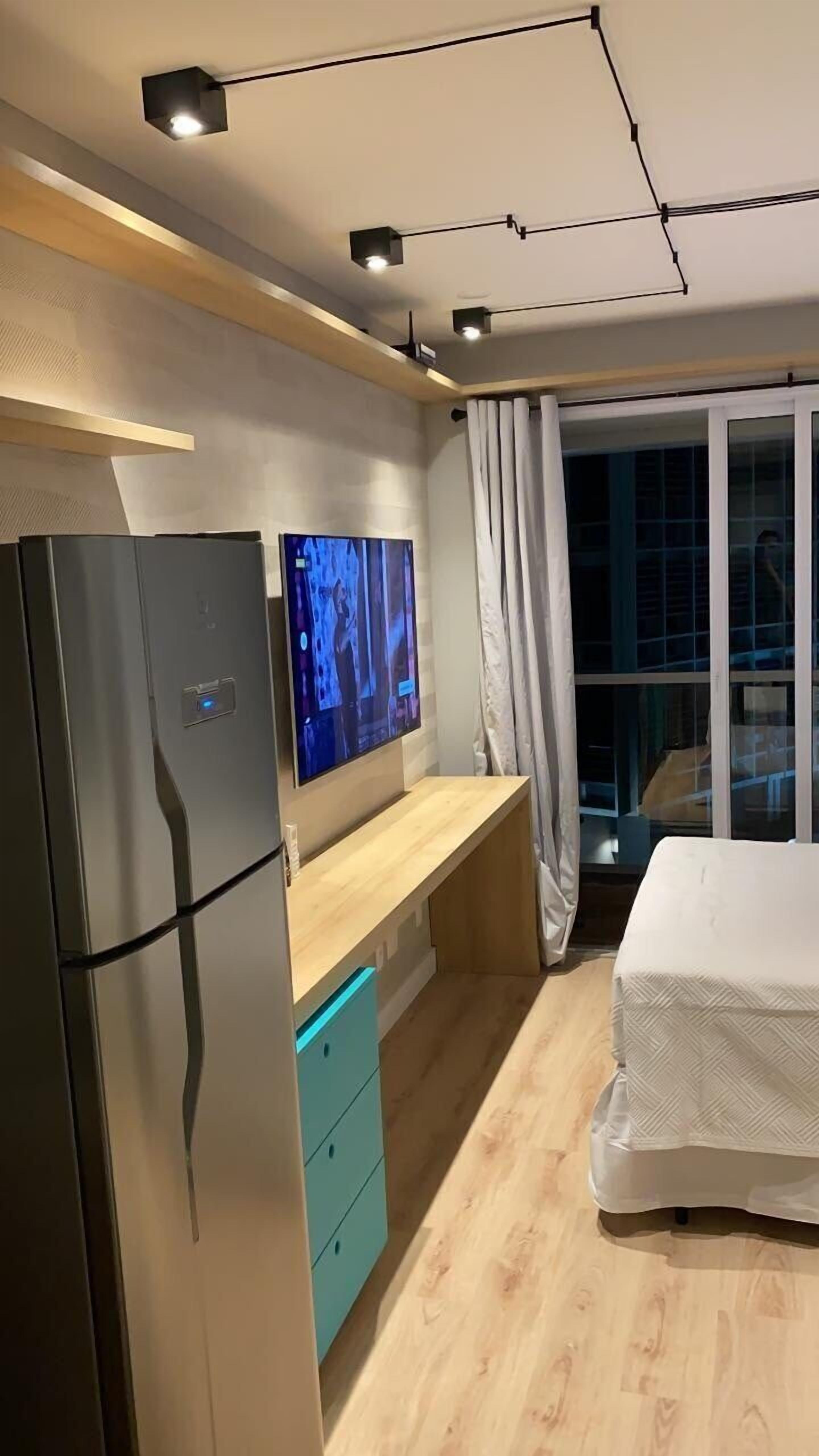 Um quarto moderno com uma cama, televisão, frigorífico e secretária de madeira.