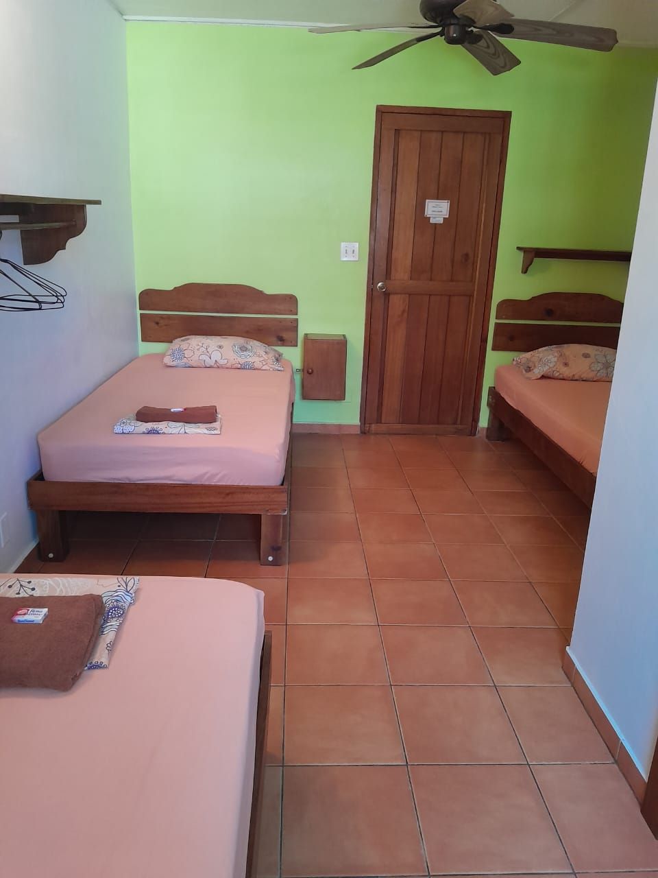 A room with two beds, a wooden door, and a ceiling fan.