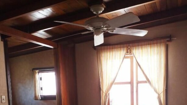 A single bed in a room with wooden beams, a ceiling fan, and a window with curtains. - HOSTAL HANSI BOCAS TOWN (Bocas del Toro)