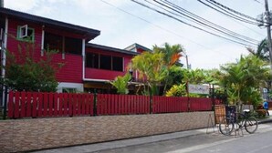 A red building with a red fence, a stone wall, and a bicycle parked outside. - HOSTAL HANSI BOCAS TOWN (Bocas del Toro)