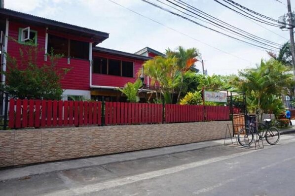 A red building with a red fence, a stone wall, and a bicycle parked outside. - HOSTAL HANSI BOCAS TOWN (Bocas del Toro)