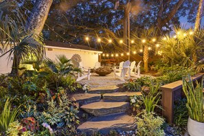 A garden with stone steps leading to a seating area, surrounded by various plants and a string of lights.