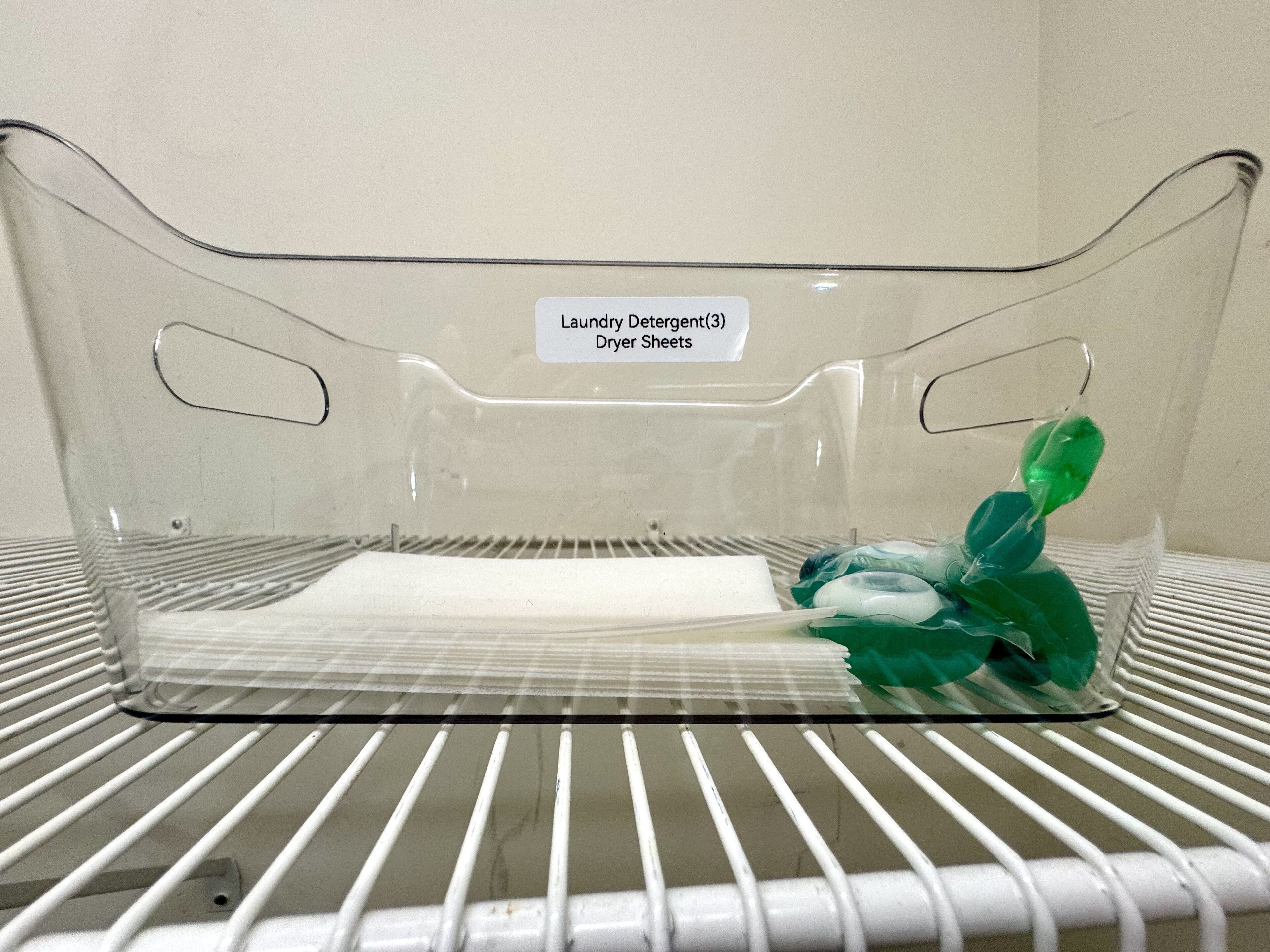 A clear plastic laundry basket with a label indicating it contains laundry detergent and dryer sheets.