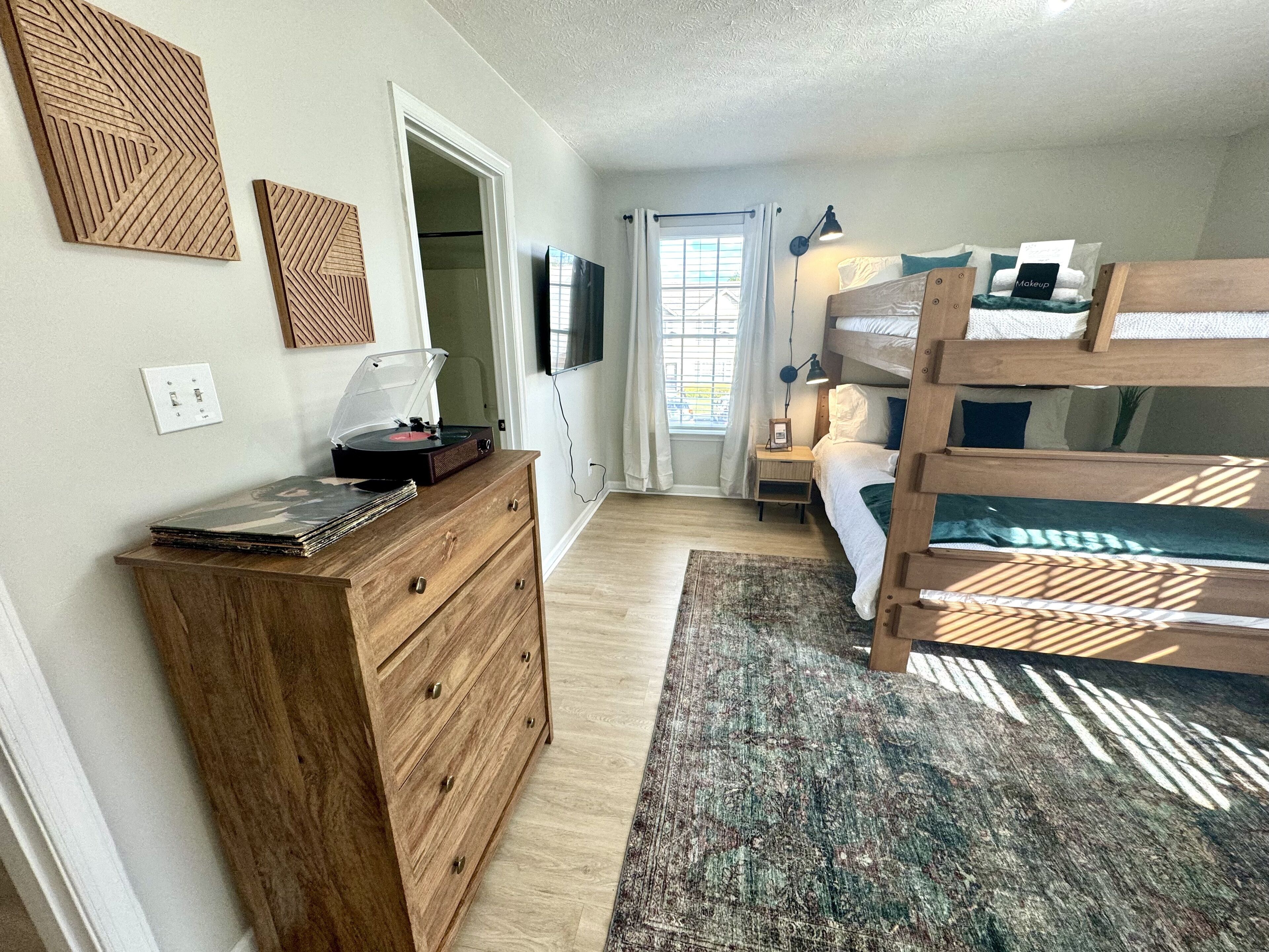 Un dormitorio con cómoda de madera, literas, televisor y ventana con cortinas.