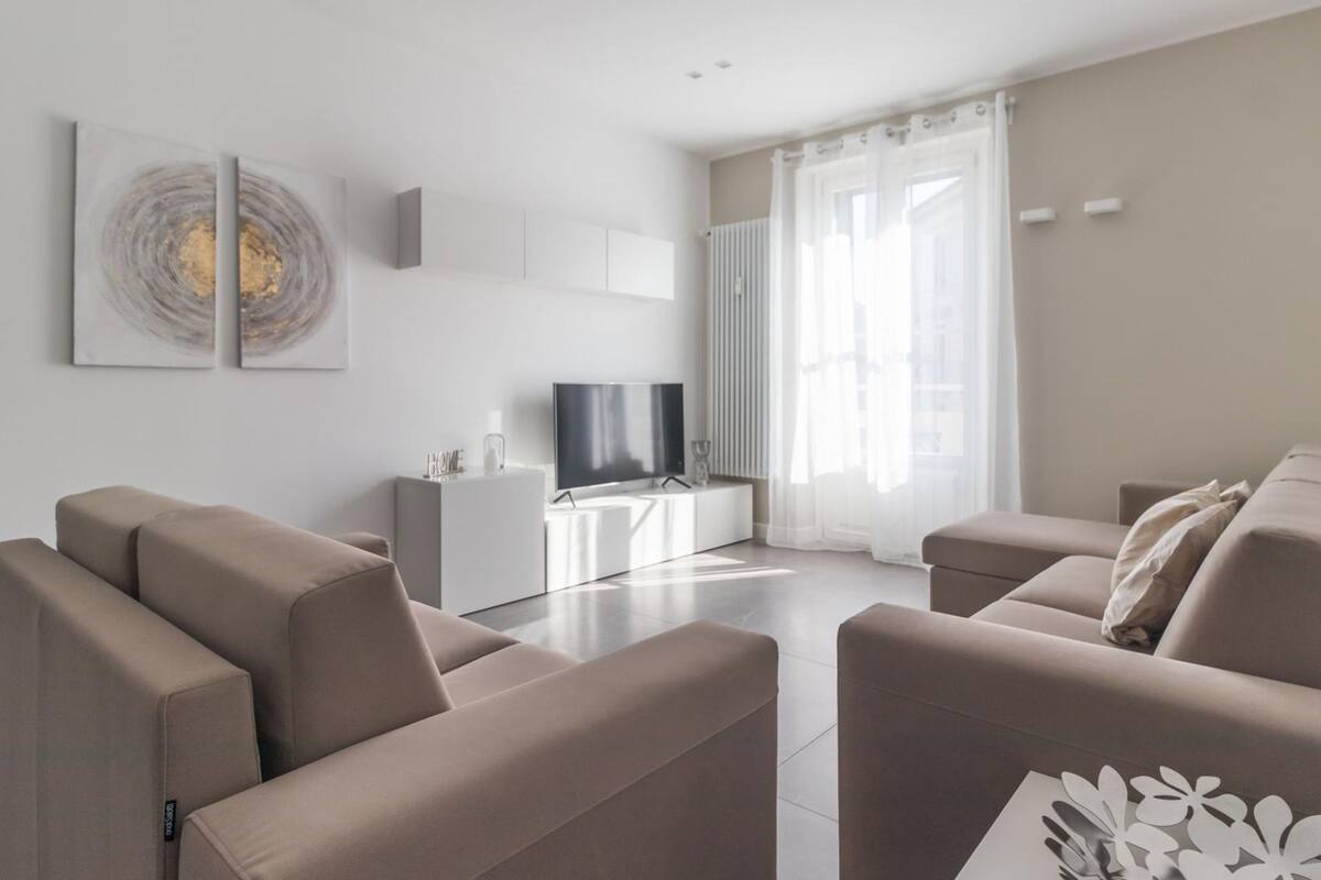 A modern living room with a sofa set, a TV on a white console, and artwork on the wall.