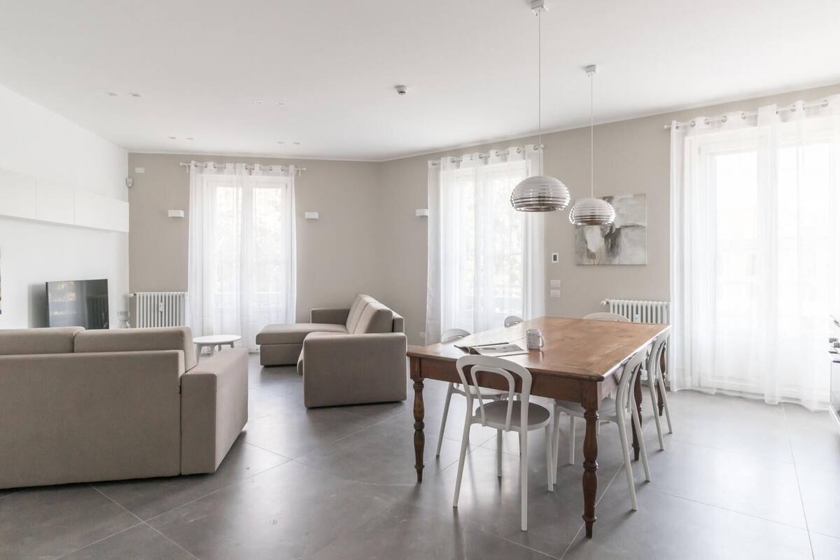 A modern living room with a sofa, a dining table with chairs, and a kitchen area with a stove.