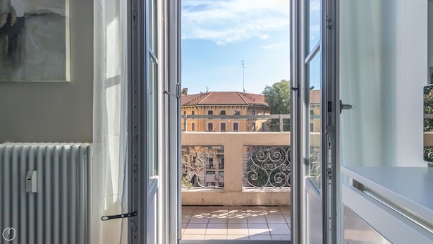An open balcony door with a view of a building with a tiled roof and a balcony with iron railings. - Italianway - Vincenzo Monti 29 (Milan)