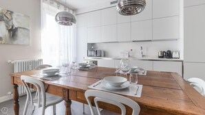 A modern kitchen with white cabinetry, a wooden dining table set for four, and a hanging pendant light. - Italianway - Vincenzo Monti 29 (Milan)