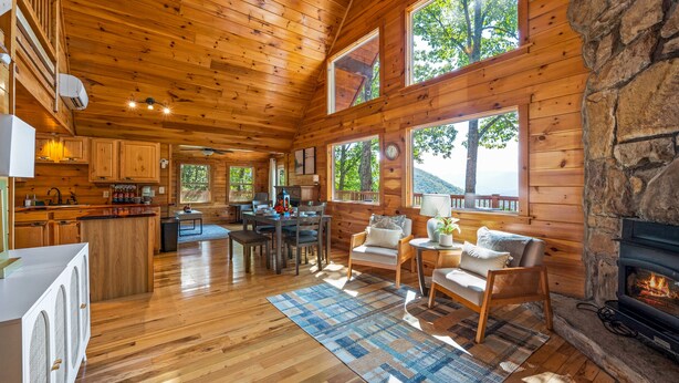 A cabin with wooden walls, a stone fireplace, a dining area, and large windows. - Top of the Smoky Mountain Views, Hot Tub + 10ft Projector (Sevierville)